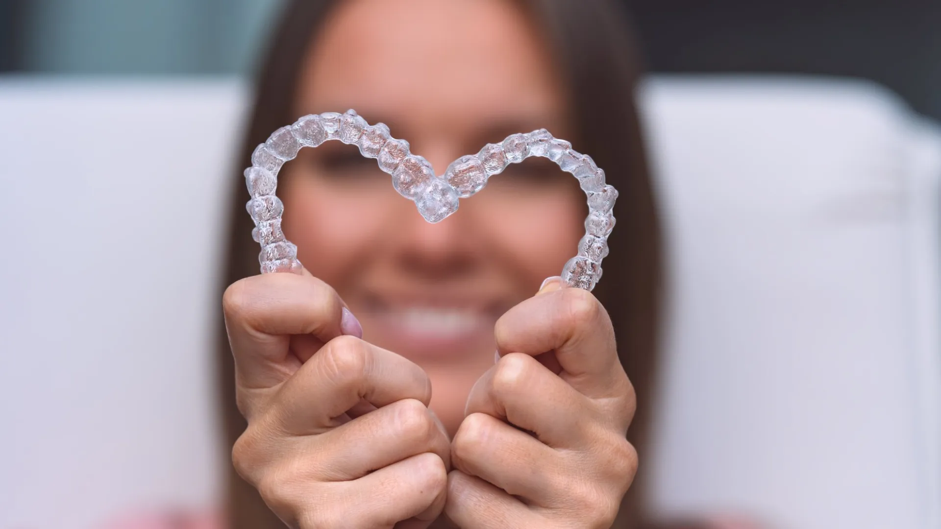Smiling patient holding two Invisalign clear aligners in a heart shape